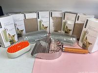 Full lot showing eight boxed wall corner wipe self groomers, three loose grey brushes, metal scoop, orange grooming brush