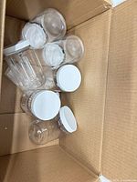 Cardboard shipping box containing several clear plastic jars with white lids