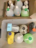 Cardboard box and plastic bin containing assorted gallon jugs of automotive and cleaning liquids