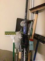 Group of brooms, mops, duster and poles leaning against wall