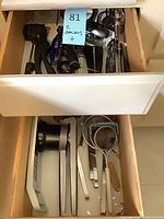 Open drawers showing assorted utensils including tongs, spatulas, strainers, meat tenderizer, apple slicer and more