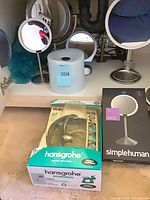 Lot overview showing hansgrohe shower set box, simplehuman mirror box, Sharper Image mirror, simplehuman toilet paper cover