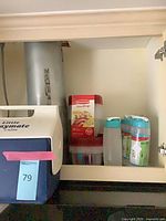 Cooler, Rubbermaid TakeAlongs box, stacked containers, and shrink-wrapped bottles inside cupboard