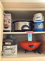 Cabinet view showing Crock-Pot, Coleman jug, KitchenAid box, Toastmaster mixer box, Braun coffee maker box, orange wok