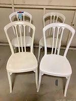 Four white molded plastic slat-back dining chairs front view