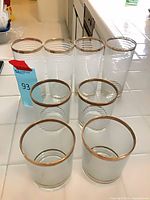 Eight striped glass tumblers arranged by height showing frosted stripes and worn gold rims