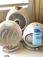 Three white portable electric heaters on windowsill.