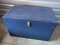 Closed blue wooden chest front view showing latch and paint wear