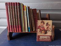 Overall lot: wood bookshelf bench holding books, plus Hershey’s cookbook in front