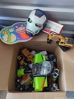 Overall view of box contents including balancing board, helmet, excavator and other toys