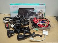 Lot overview showing boxed Logitech K400 keyboard, assorted cables in bundle and tray