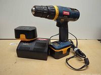 Drill standing on battery mounted to base, charger and extra battery visible
