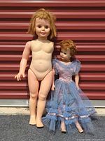 Two dolls standing by red backdrop, size comparison