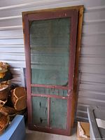 Full view of burgundy wood screen door leaning against wall