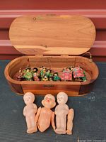 Overall shot showing open wooden box, miniature ornaments inside, and three dolls in front
