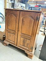 Front view of closed cabinet showing paneled doors, hinges, bracket feet
