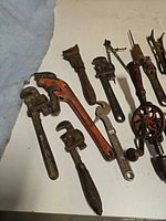 Group showing several pipe wrenches, adjustable wrench and eggbeater drill