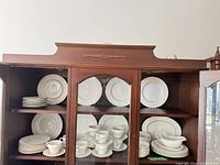China cabinet shelves with ridged-edge white plates, cups, saucers, gravy boat, and platter