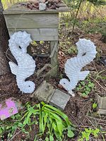 Both concrete seahorse statues leaning against garden structure
