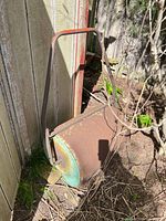 Full view of rusted steel lawn roller leaning against fence