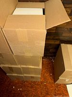 Stack of brown cardboard boxes, top box open revealing white paper reams