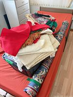 Overall lot on bed showing basket of folded fabrics and two rolled upholstery fabrics