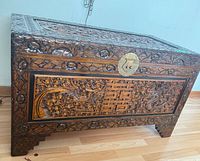 Full view of carved wooden chest showing lid, front panel carving, feet