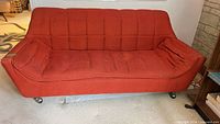 Full front view of red-orange tufted sofa on metal legs