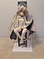 Front view of figure seated on chair on display base