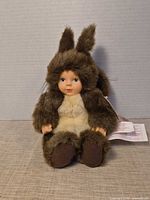 Front view of doll sitting upright showing costume, face, hands, tag partially visible