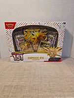 Front view of sealed Zapdos ex Collector Tin showing contents and Scarlet & Violet 151 branding