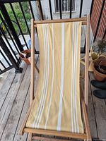 Front view of wooden folding deck chair with yellow and white striped canvas sling