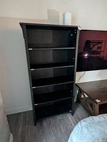 front view of black six-shelf bookcase next to TV stand