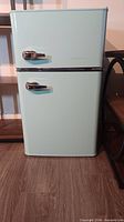 Full view of mint aqua Insignia compact refrigerator with two doors and chrome handles