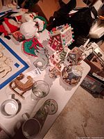 Tabletop view showing full assortment: village houses, plush figures, glasses, mugs, wicker sleigh