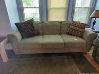 Front view of beige three-seat sofa with two throw pillows