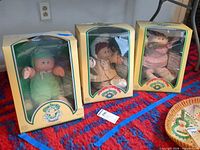 Three boxed Cabbage Patch Kids Preemie dolls in green, tan and pink outfits
