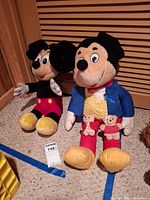 Two Mickey Mouse plush toys side by side on floor