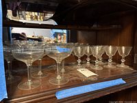Group of clear stemmed champagne coupes on upper cabinet shelf