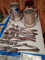 Flatware pieces laid out with two pewter tankards visible