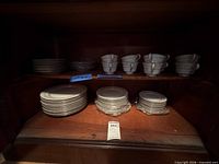 Stacked dinner and side plates, cups on shelf