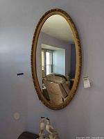 Full view of oval gold gilded wall mirror on wall