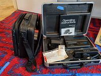 Camcorder in open hard case with accessories, soft bag alongside