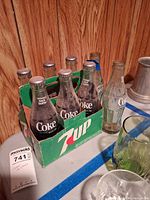 Six capped Coca-Cola bottles in 7UP carrier, dusty condition