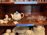 Shelf view showing porcelain teapot with rose design, pink depression glass cups and compote