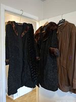 Two outerwear pieces: black fur coat with brown mink trim and brown leather coat hanging