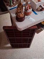 Wooden compartment tray leaning against table with figurines visible above