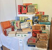 Full group of roughly 25 vintage jigsaw puzzle boxes displayed on tiered surface