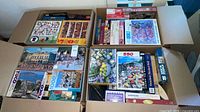 Two open U-Haul cartons filled with assorted jigsaw puzzle boxes