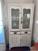 Full front view of distressed white china cabinet with glass doors, drawers, and carved lower doors